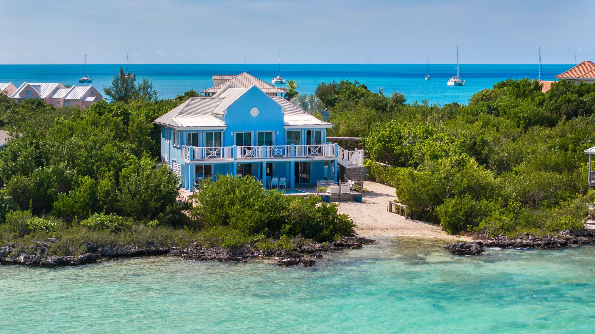 Juan Del Mar, a two storey blue villa on its own shoreline at Chalk Sound, seen from the water
